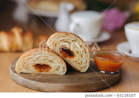 Two halves of freshly bared croissant on wooden board with delotious homemade apricot jam. Background of cappuccino. Morning breakfast 65116107