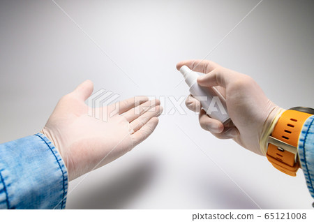 Close-up self-treatment of hands with an antiseptic with an aerosol first-person view. Men's hands in white medical gloves, a blue denim shirt Close-up self-treatment of hands with an antiseptic with an aerosol first-person view. Men's hands in white medical gloves, a blue denim shirt 65121008