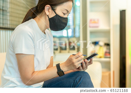 Woman in protective mask working on smart phone using digital pen. 65121188