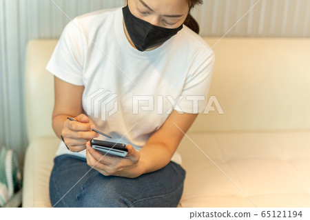 Woman in protective mask working on smart phone using digital pen. 65121194