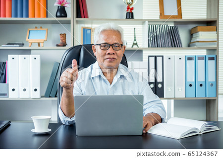 Happy Asian elderly man sitting in front of a Happy Asian elderly man sitting in front of a 65124367