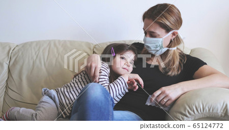 sick mother with surgical mask stay with her child on the sofa 65124772