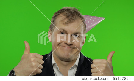 Drunk sleepy young businessman with hangover in festive cap giving thumbs up Drunk sleepy young businessman with hangover in festive cap giving thumbs up 65127893
