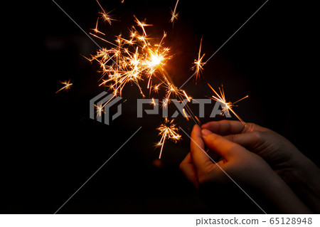 Female hand holding a burning sparkler, Christmas Female hand holding a burning sparkler, Christmas 65128948