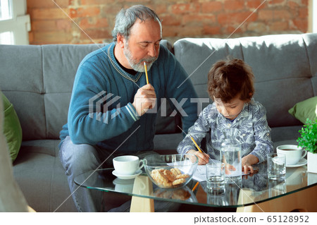 Grandfather and his grandson spending time insulated at home, stadying, writing, drawing or playing together 65128952