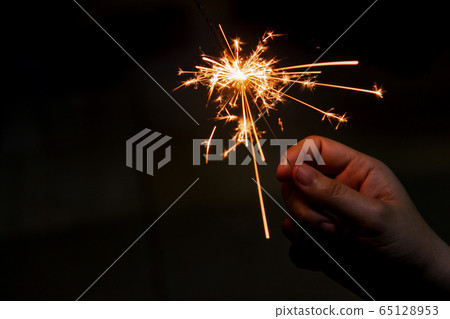 Female hand holding a burning sparkler, Christmas Female hand holding a burning sparkler, Christmas 65128953