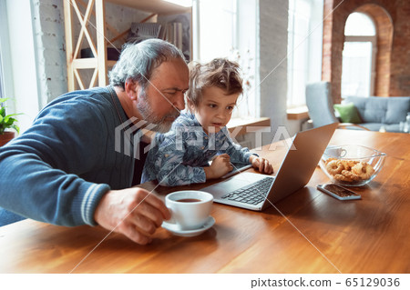 Grandfather and his grandson spending time insulated at home, stadying, watching cinema, shopping together 65129036