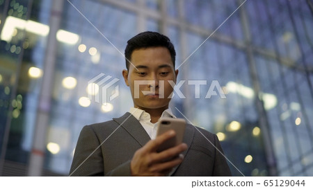 Low angle view of a young asian businessman, leading correspondence on the phone. Downtown district. 65129044