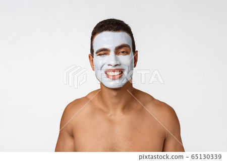 Picture of cheerful nice young african guy smiling on camera. Portrait of man with cream mask on cheeks. Beauty routine 65130339