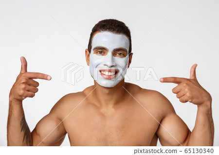Photo of shirtless african american man smiling and applying face cream isolated over white background 65130340