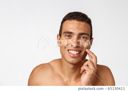 Photo of shirtless african american man smiling and applying face cream isolated over white background Photo of shirtless african american man smiling and applying face cream isolated over white background 65130411