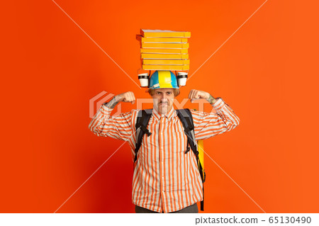 Contacless delivery service during quarantine. Man delivers food and shopping bags during insulation. Emotions of deliveryman isolated on orange background. Contacless delivery service during quarantine. Man delivers food and shopping bags during insulation. Emotions of deliveryman isolated on orange background. 65130490