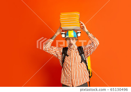 Contacless delivery service during quarantine. Man delivers food and shopping bags during insulation. Emotions of deliveryman isolated on orange background. Contacless delivery service during quarantine. Man delivers food and shopping bags during insulation. Emotions of deliveryman isolated on orange background. 65130496