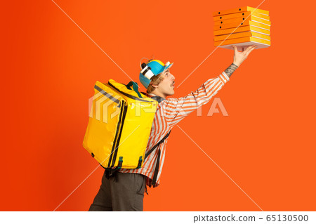 Contacless delivery service during quarantine. Man delivers food and shopping bags during insulation. Emotions of deliveryman isolated on orange background. 65130500