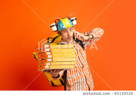 Contacless delivery service during quarantine. Man delivers food and shopping bags during insulation. Emotions of deliveryman isolated on orange background. Contacless delivery service during quarantine. Man delivers food and shopping bags during insulation. Emotions of deliveryman isolated on orange background. 65130529