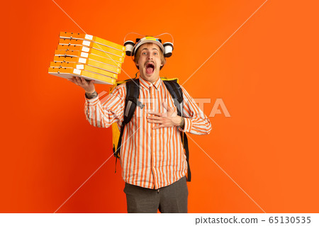 Contacless delivery service during quarantine. Man delivers food and shopping bags during insulation. Emotions of deliveryman isolated on orange background. Contacless delivery service during quarantine. Man delivers food and shopping bags during insulation. Emotions of deliveryman isolated on orange background. 65130535