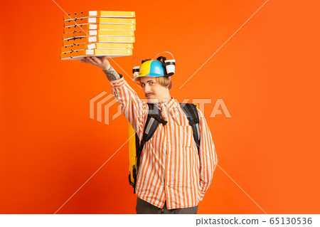 Contacless delivery service during quarantine. Man delivers food and shopping bags during insulation. Emotions of deliveryman isolated on orange background. 65130536