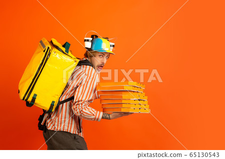 Contacless delivery service during quarantine. Man delivers food and shopping bags during insulation. Emotions of deliveryman isolated on orange background. 65130543