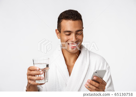 An attractive man drinking a glass of water against white background An attractive man drinking a glass of water against white background 65130758