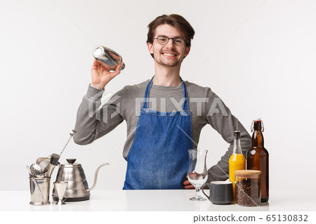 Barista, cafe worker and bartender concept. Portrait of happy friendly young male employee smiling to customer shaking shaker to make special drink near bar counter, prepare coffee 65130832
