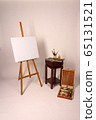Oil painting. Blank canvas on Easel. Palette with paints and brushes. Squeeze out oil paints on a palette. Clean cloth with copy space. Set of brushes in a cup. Box with drawing tools. 65131521