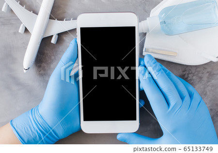 Travel planning concept, coronavirus and quarantine. Hands in disposable gloves hold smartphone Travel planning concept, coronavirus and quarantine. Hands in disposable gloves hold smartphone 65133749