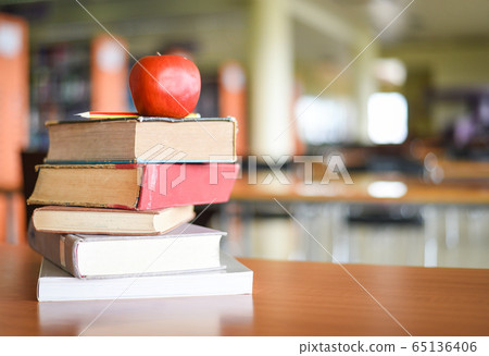 An apple on the books on the table with bookshelf An apple on the books on the table with bookshelf 65136406