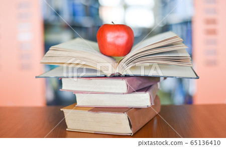 An apple on the books on the table with bookshelf An apple on the books on the table with bookshelf 65136410