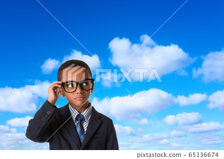 thoughtful african american boy in business suit with glasses over blue sky background. 65136674