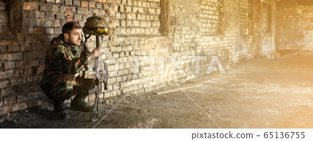 A male military soldier squatting took off his helmet and hung on the barrel of a machine gun 65136755