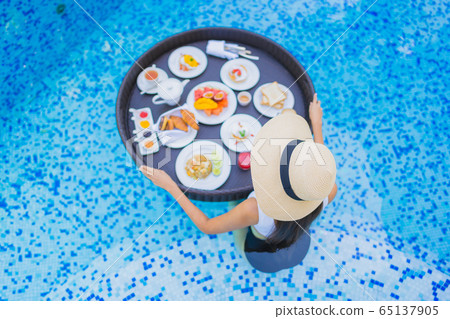 Portrait beautiful young asian woman happy smile with floating breakfast in tray on swimming pool 65137905