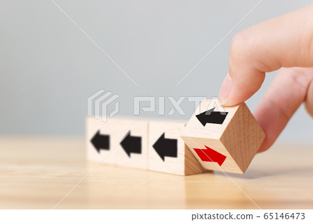 Hand flip over wooden cube block with red arrow facing the opposite direction black arrows 65146473