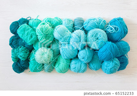 Yarn of green, turquoise, aquamarine and blue colors. White wood background. Knitting needles and crochet hooks. Scissors. White background. Yarn of green, turquoise, aquamarine and blue colors. White wood background. Knitting needles and crochet hooks. Scissors. White background. 65152233