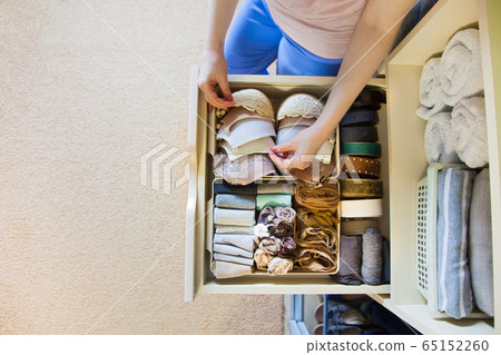 The woman folds Underwear and bra in the drawer. A woman is tidying up the closet. Vertical storage of clothing The woman folds Underwear and bra in the drawer. A woman is tidying up the closet. Vertical storage of clothing 65152260