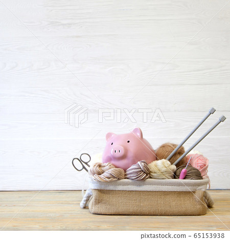 Colored yarn. Knitting needles. Pig piggy bank with glasses. Wooden background. 65153938