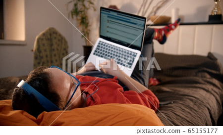 Young man lying on the bed and searching the internet 65155177
