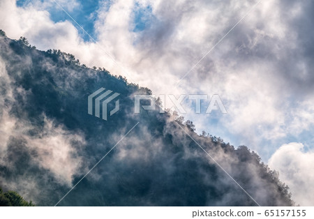High mountains with green slopes and rocks hidden in thick clouds and fog High mountains with green slopes and rocks hidden in thick clouds and fog 65157155