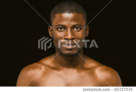 Nude smiling African macho man posing on black background, portrait of an attractive African american man smiling slightly while looking at the camera. Toned image Nude smiling African macho man posing on black background, portrait of an attractive African american man smiling slightly while looking at the camera. Toned image 65157535