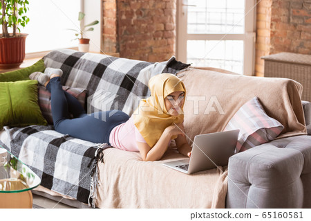 A pretty young muslim woman at home during quarantine and self-insulation, using laptop, listen to music, watching cinema, serials, shopping, studying A pretty young muslim woman at home during quarantine and self-insulation, using laptop, listen to music, watching cinema, serials, shopping, studying 65160581