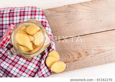 Opened glass jar with ginger water on red tartan cloth on diagonal wooden boards. Trendy healthy detox isotonic drink. Natural infusion for normalization of metabolism and weight. Top view, copy space 65162270