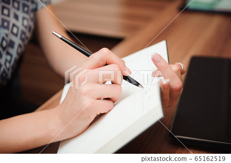 Closeup of a female hand writing on an blank notebook with a pen. Closeup of a female hand writing on an blank notebook with a pen. 65162519