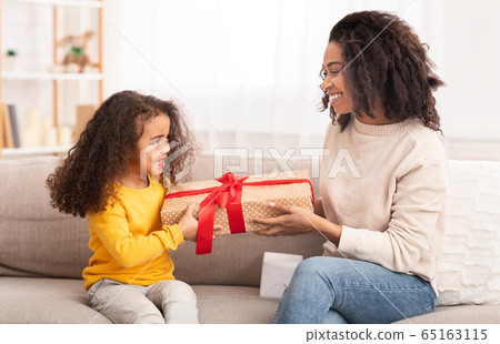 Daughter Giving Gift To Mom Sitting On Couch At Home 65163115