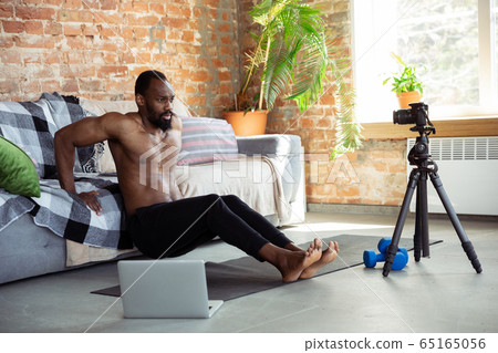 Young african-american man teaching at home online courses of fitness, aerobic, sporty lifestyle during quarantine, reording on camera, streaming 65165056