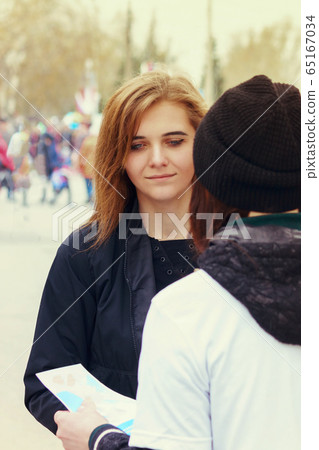 The agitator on the street offers a passer-by to a girl to take a leaflet. 65167034