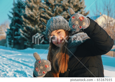 Beautiful Caucasian girl with loose hair in a knitted hat, scarf and mittens outdoors  65167035