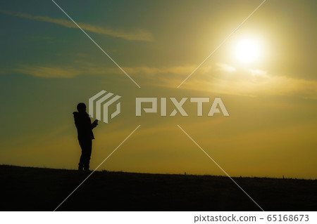 一個男人站在一座小山在日落時的剪影 一個男人站在一座小山在日落時的剪影 65168673