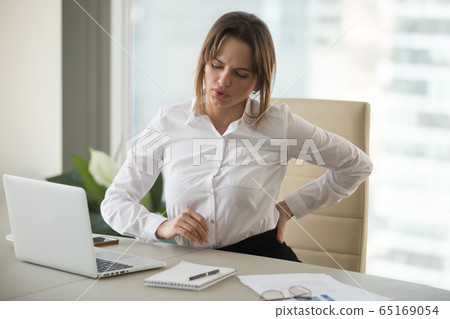 Upset businesswoman feeling back pain touching aching muscles in 65169054