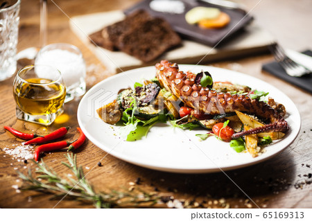 Warm octopus salad with stir fried vegetables and aji sauce on white plate. Delicious healthy mediterranean traditional seafood closeup served on a table for lunch. Warm octopus salad with stir fried vegetables and aji sauce on white plate. Delicious healthy mediterranean traditional seafood closeup served on a table for lunch. 65169313