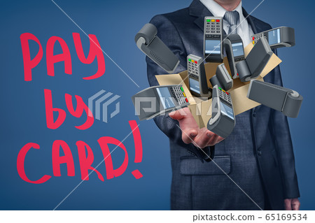 Businessman holding cardboard box filled with PIN pads and 'Pay by card' sign on blue background. Businessman holding cardboard box filled with PIN pads and 'Pay by card' sign on blue background. 65169534