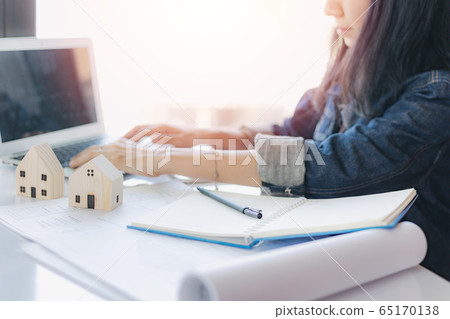 Asian woman using computer laptop with architectural plan and wooden house model 65170138